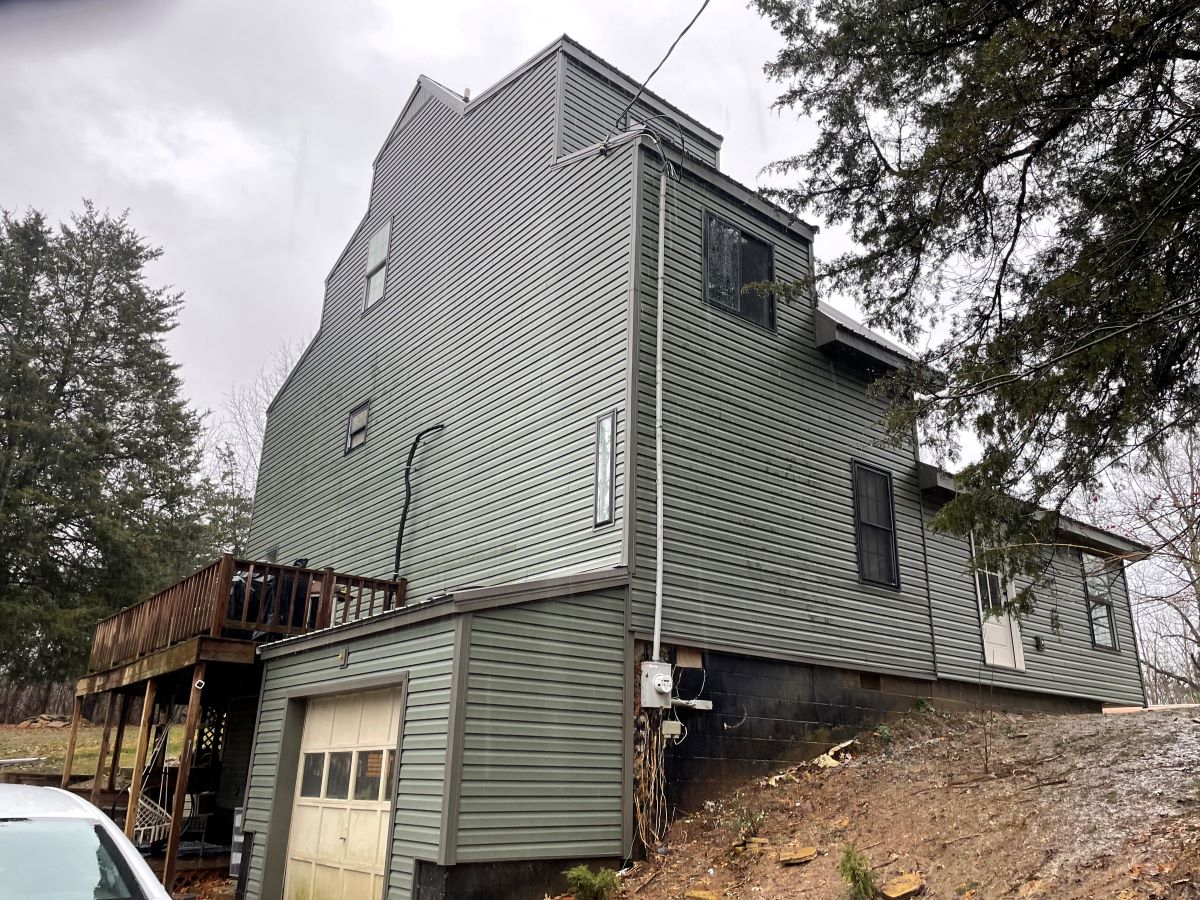 Three-story green house with wooden deck and garage.