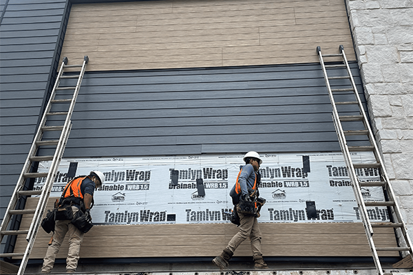 Construction workers install siding on building exterior.