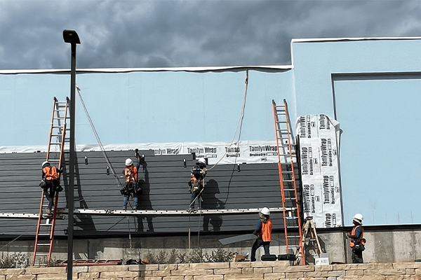 Workers installing insulation on building exterior.